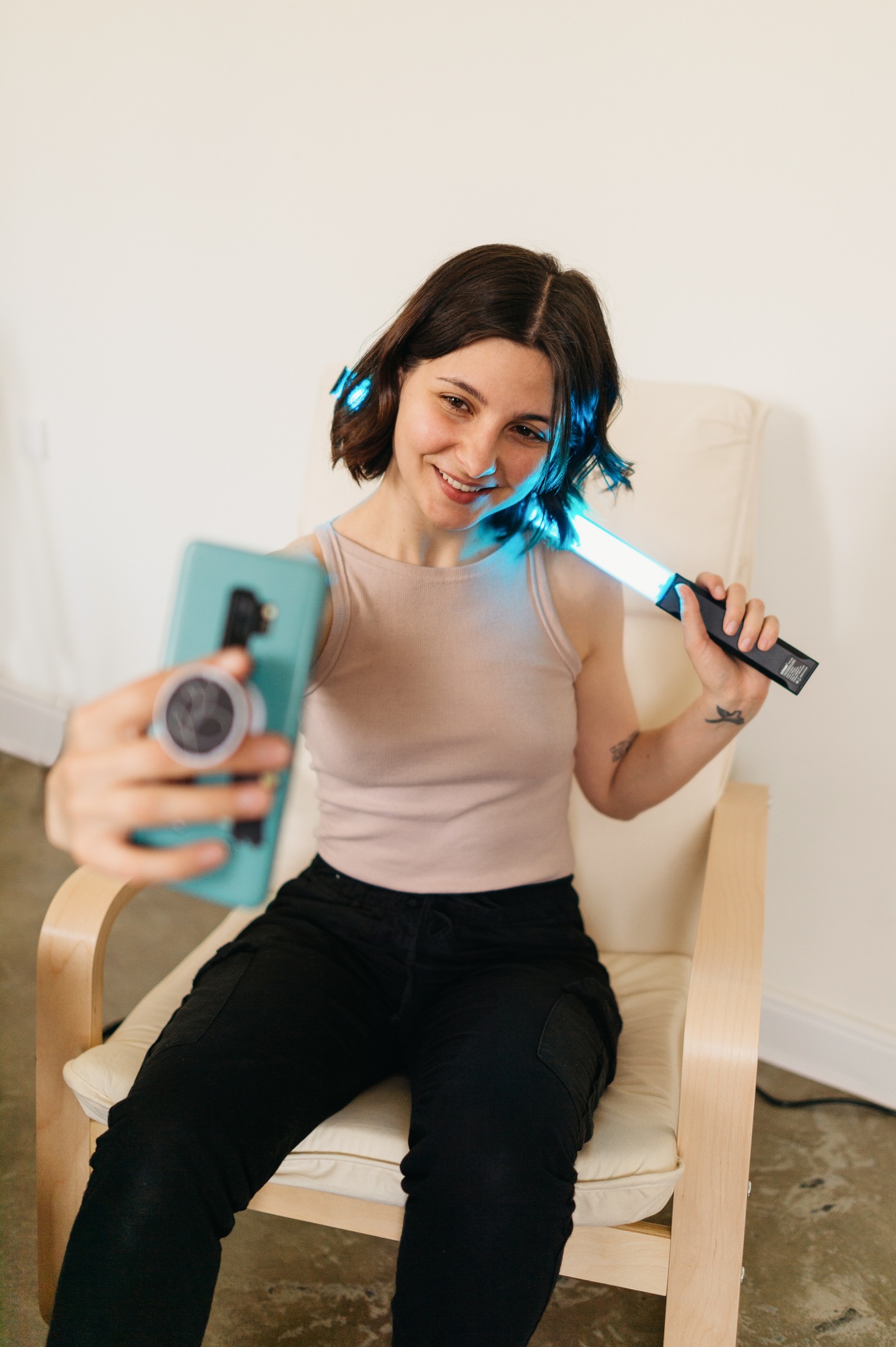 Young woman making photo or video on mobile phone using special light stick at home, influencer